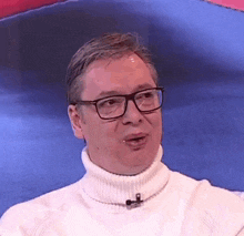a man wearing glasses and a white turtleneck sweater is talking