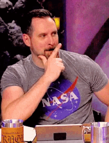 a man wearing a nasa t-shirt is sitting in front of a laptop