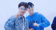 two young men wearing glasses and a blue hoodie are standing next to each other and looking at something .