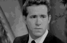 a black and white photo of a man in a suit and tie looking at the camera .