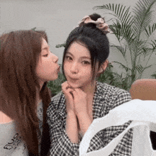 a woman kissing another woman on the cheek in front of plants
