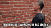 a man standing in front of a brick wall with the words " anything but working on ego legacy " on the bottom