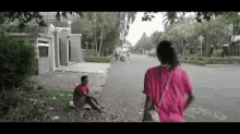 a man is sitting on the side of the road while a woman walks down the street .