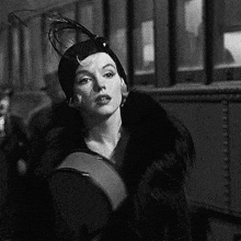 a black and white photo of a woman wearing a feathered hat and fur coat .