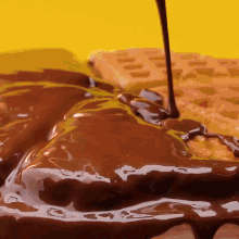 chocolate is being poured over a waffle on a yellow surface