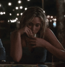 a woman sitting at a table with a drink in her hand and a ring on her finger