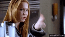 a woman with long red hair is standing in front of a refrigerator and making a funny face .