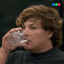 a man drinking a glass of water with a green blue and pink circle in the background