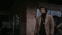 a man in a paisley jacket and black turtleneck stands in front of a store window