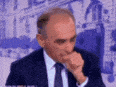 a man in a suit and tie is coughing while sitting in front of a building .