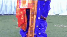 a woman in a blue and red dress is standing on a grassy field