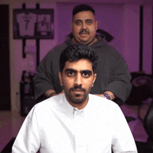 a man in a white shirt is getting his hair cut by a man in a grey hoodie with the number 7 on it