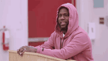a man in a pink hoodie is leaning on a wooden podium
