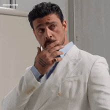 a man in a white suit and tie is covering his mouth with his hand