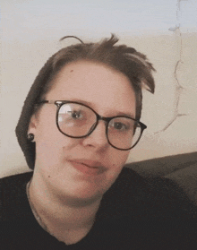 a woman wearing glasses and a beanie is smiling for the camera