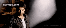a man in a black jacket is standing in a dark room looking at the camera .