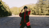 a man in a black jacket and red tie is standing in a field holding a sword .