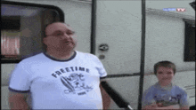 a man wearing a freetime shirt stands in front of a camper