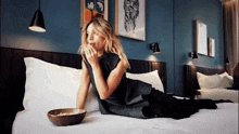 a woman sits on a bed with a bowl of popcorn