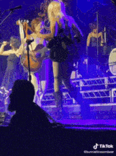 a woman is holding a guitar while standing on a stage with other people .