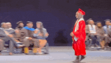 a graduate in a red cap and gown is walking on stage