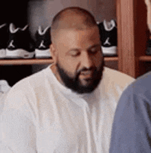 a man with a beard is wearing a white shirt and talking to another man in a room .