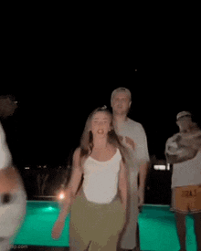 a woman is dancing in front of a swimming pool at night .