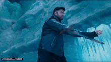 a man in a leather jacket is holding a sword in front of an ice cave