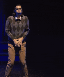 a man in a plaid sweater and brown pants stands on a stage