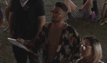 a man in a hawaiian shirt stands next to a woman in sunglasses