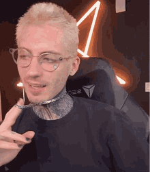 a man wearing glasses and a chain around his neck is sitting in a chair .