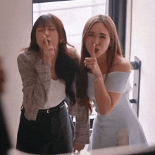 two women are standing next to each other and one is making a shhh gesture