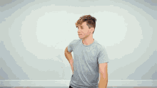a young man in a grey t-shirt is standing in front of a wall