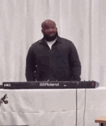 a man is standing in front of a roland electronic keyboard .