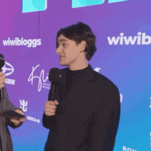 a man in a suit stands in front of a wall that says ' wiwibloggs ' on it