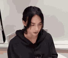 a young woman in a black hoodie is sitting at a table .