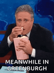 a man eating popcorn with the words meanwhile in greenburgh