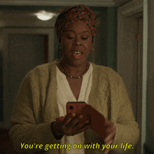 a woman in a yellow sweater is looking at her phone and says you 're getting on with your life