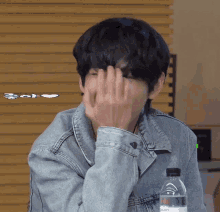 a man in a denim jacket is covering his face with his hands