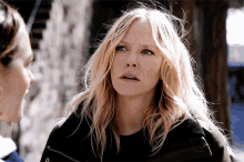 a woman with blonde hair and a black jacket looks at the camera