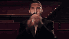 a man with a beard wearing a tuxedo and bow tie is sitting in a theater .