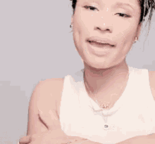 a woman wearing a white tank top and a necklace is pointing at the camera .