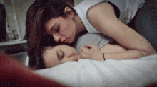 two women are laying on a bed and one is kissing the other on the cheek .