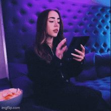 a woman sitting on a couch looking at her phone with a bowl of chips next to her