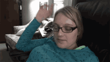 a woman wearing glasses and a blue sweater is sitting in a chair