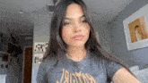 a woman wearing a gray t-shirt with the word justice on it is taking a selfie in a room .