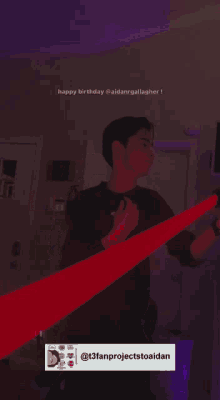 a man in a black shirt is dancing in a room with a purple light behind him .