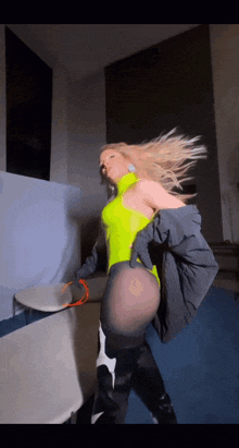 a woman in a neon yellow bodysuit and black boots dancing