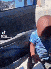 a baby is sitting in the back seat of a car with his head in the door .