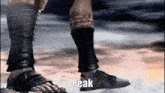 a person wearing sandals and socks is standing on a rock and the word peak is on the screen .